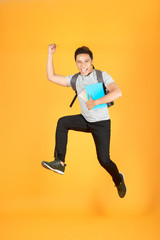 Excited young Asian man jumping with a backpack on the an orange background