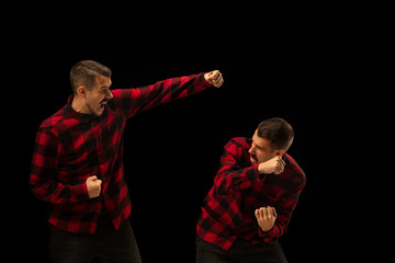 Young handsome man arguing with himself on black studio background. Concept of human emotions,...