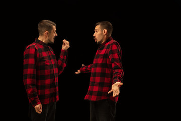 Young handsome man arguing with himself on black studio background. Concept of human emotions, mental issues, internal conflict, split personality. Half lenght portrait. Negative space.