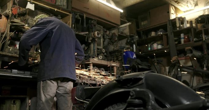 A motorcycle repair mechanic works as a grinder in his old vintage garage near a motorcycle
