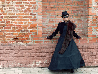 Fototapeta na wymiar girl in a black dress on a background of a brick wall in autumn