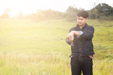 Portrait of asian man are standing on road  with blurred of grass field on the background. Man in a Jean jecket are standing and enjoying the beautiful nature.