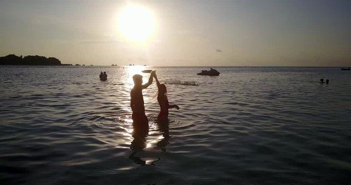 Lovely young couple dancing in the water, with girl spinning, during sunset at tropical paradise