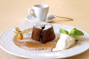 chocolate fondant on a white plate, ice cream and a cup on the background