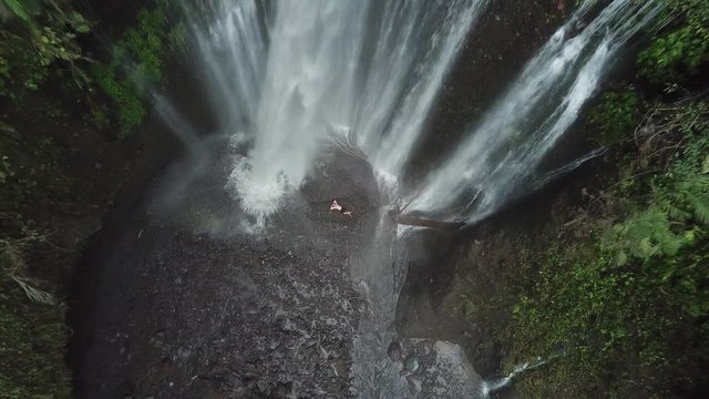 Male Laying Under Tropical Tiu Kelep Waterfall in Rainforest of Lombok Island Indonesia, Top Down Ascending Aerial