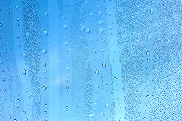 Naklejka na ściany i meble Water droplets on the glass with a blue background.