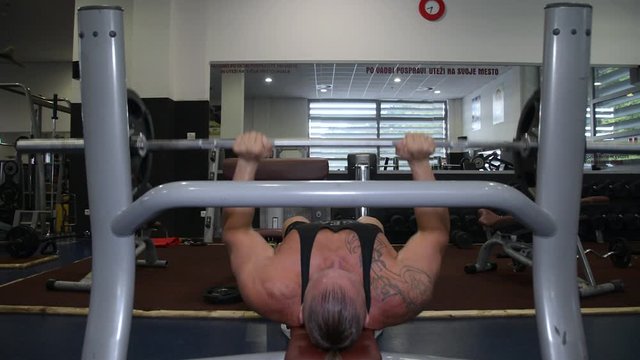 Close up, strong tattooed muscular bodybuilding man doing barbell bench press chest muscle repetition workout exercise in gym