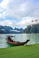 Fototapeta na wymiar Wooden boat in lake with mountain range and clouds background