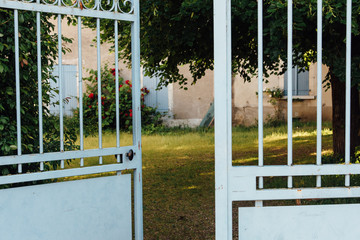 un vieux portail bleu vert en fer forgé ouvert sur un joli jardin, une cour et une maison de campagne bleue