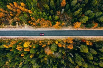 Aerial view of rural road in yellow and orange autumn forest in rural Finland.