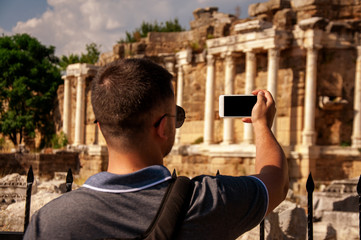 Tourist man photographs ancient monuments on the phone. The image in the photo and on the phone. Sunny hot day. Travels.