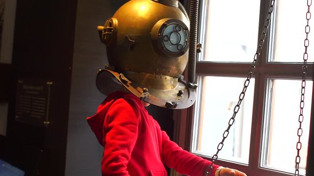 A boy is standing in an old scuba diver helmet.