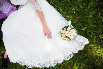 bride and groom sitting on grass with beautiful bouquet