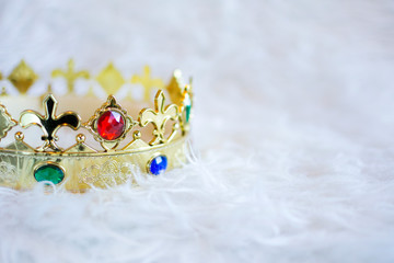 Gold crown with colored gems on white hairy background. Copyspace right.