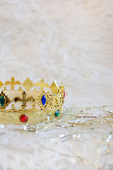 Golden crown with colored gems and golden ornaments on white cloth background. Vertical. 