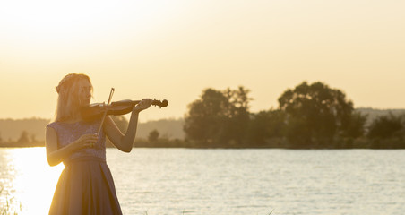 romantic silhouette of young woman with a violin at dawn on river bank, elegant girl playing a musical instrument on nature, concept music and inspiration