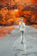 Fototapeta premium back of young woman in sportswear running distance on asphalt road, girl engaged in sport outdoors on autumn day, concept healthy lifestyle and bodycare