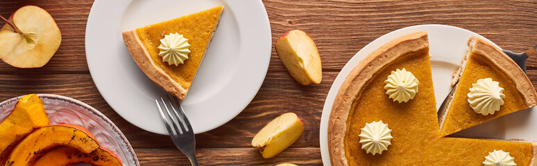 panoramic shot of cut pumpkin pie with whipped cream near baked pumpkin, fork, and cut apples on brown wooden table