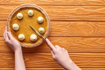 cropped view of woman cutting delicious pumpkin pie with whipped cream on orange wooden table