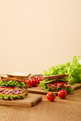 selective focus of fresh sandwich near lettuce, bread, cherry tomatoes on wooden table isolated on beige