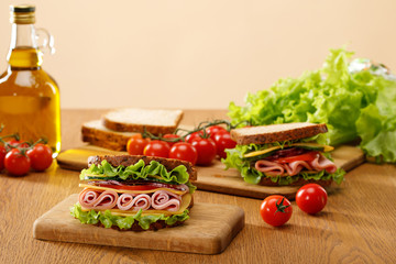 selective focus of fresh sandwich near lettuce, bread, cherry tomatoes and oil on wooden table isolated on beige