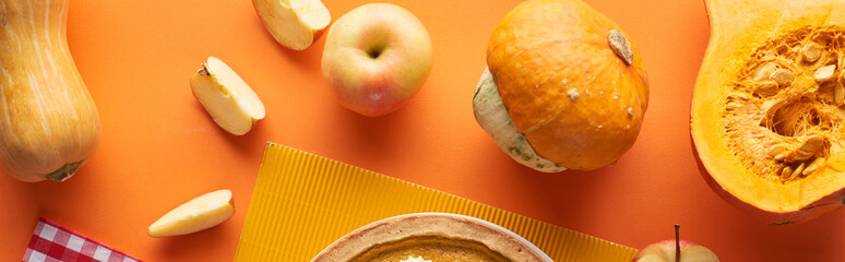 fresh, whole and cut pumpkins and apples near textured napkin on orange surface