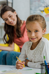 selective focus of happy kid studying near babysitter at home