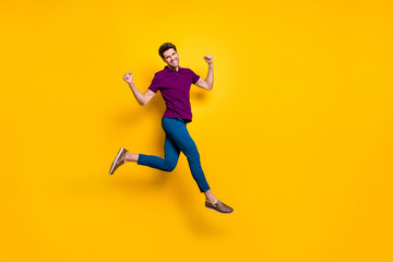 Fototapeta na wymiar Full length body size photo of cheerful positive strong man running jumping demonstrating his powerful muscles wearing blue pants trousers purple t-shirt isolated over vivid color background