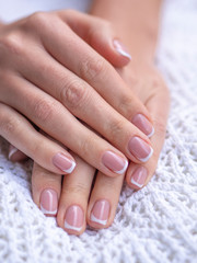 Close up vertical shot of beautiful woman's hands on table showing nails with french manicure