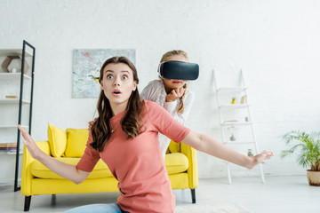 surprised babysitter with outstretched hands near kid in virtual reality headset