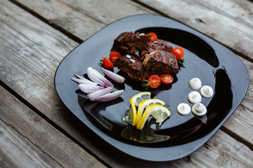 Restaurant food. Pork combined with vegetables on a black plate. On the wooden floor.