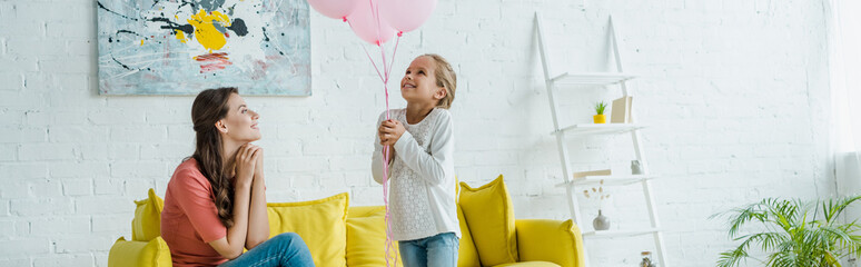 panoramic shot of cheerful babysitter looking at pink balloons near happy kid
