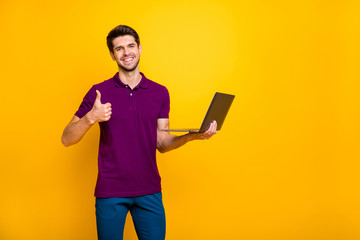 Photo of cheerful positive nice attractive man showing you thumb up holding laptop wearing blue pants trousers isolated over yellow vivid color background