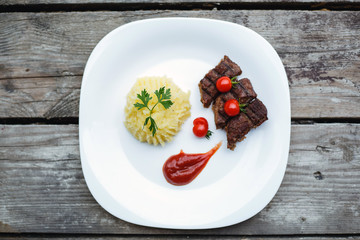 Restaurant food. Pure potatoes combined with grilled pork, decorated with cherry tomatoes. On the wooden floor.