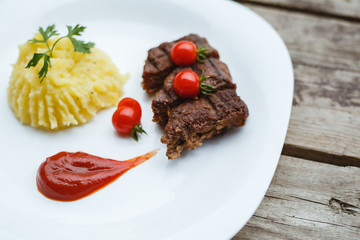 Restaurant food. Pure potatoes combined with grilled pork, decorated with cherry tomatoes. On the wooden floor.