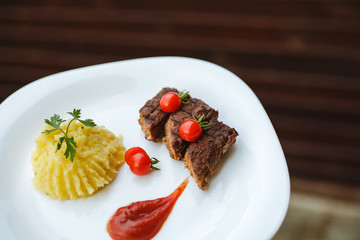Restaurant food. Pure potatoes combined with grilled pork, decorated with cherry tomatoes. On the wooden floor.