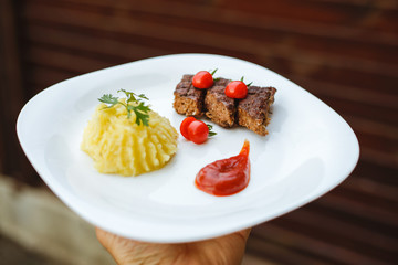 Restaurant food. Pure potatoes combined with grilled pork, decorated with cherry tomatoes. On the wooden floor.