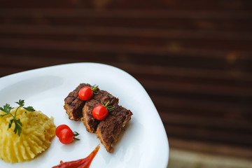 Restaurant food. Pure potatoes combined with grilled pork, decorated with cherry tomatoes. On the wooden floor.