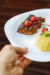 Restaurant food. Pure potatoes combined with grilled pork, decorated with cherry tomatoes. On the wooden floor.