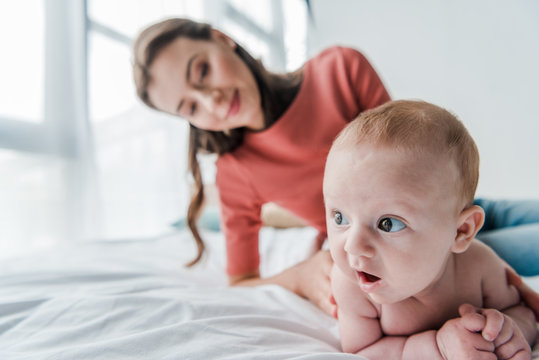 selective focus cute infant baby near happy mother in bedroom