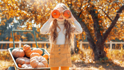 Little girl covered face with two small pumpkin