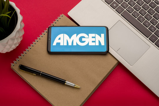Tula, Russia - october 19, 2019: Amgen Inc displayed on a smartphone near modern laptop on red background