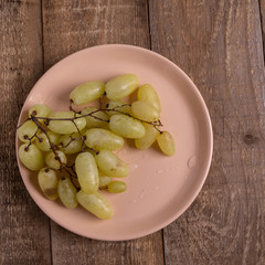 Bunch of green grapes in a plate on a wooden table.