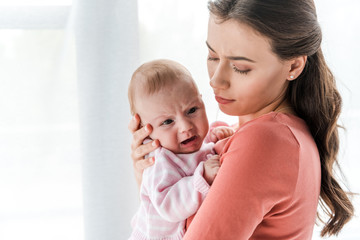 attractive woman holding in arms crying infant at home