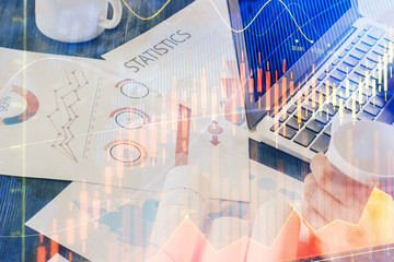 Double exposure of man's hands writing notes with laptop of stock market with forex graph background. Top View. Concept of research and trading.