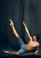 Young male ballet dancer dancing on a black fabric background. Ballet movements. Young dark-haired ballet dancer dancing on a black fabric background. Dressed in black short pants