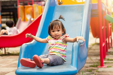 Fototapeta na wymiar Asian child girl playing a slider toy at the playground. Happy Baby aged 2 years old.