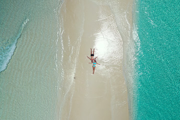 Fototapeta na wymiar Dron view of romantic couple stretched on the white sand of a maldivian beach