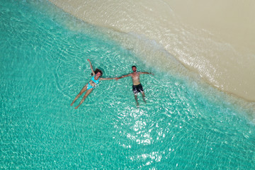 Aerial view of romantic couple floating and holding hands in turquoise water