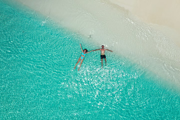 Romantic couple swiming and holding hands on beautiful white sandy beach with turquoise water from aerial view